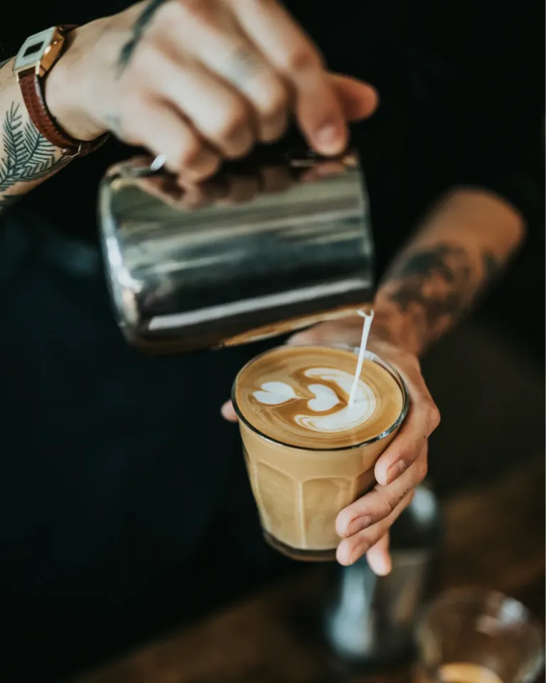 Barista gießt Milchschaum in einen Cappuccino mit Latte-Art-Verzierung.