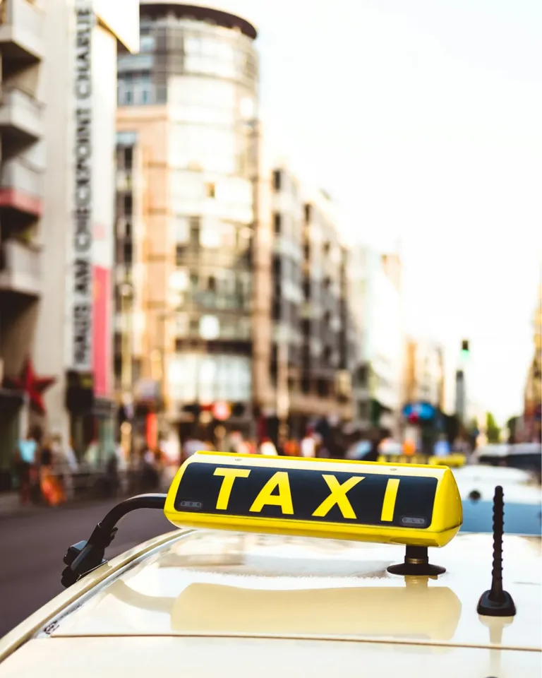 Gelbes Taxischild auf dem Dach eines blauen Taxis in einer belebten Fußgängerzone.